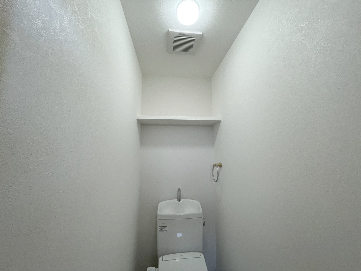 天井照明と換気扇を備えた白い壁のトイレ空間